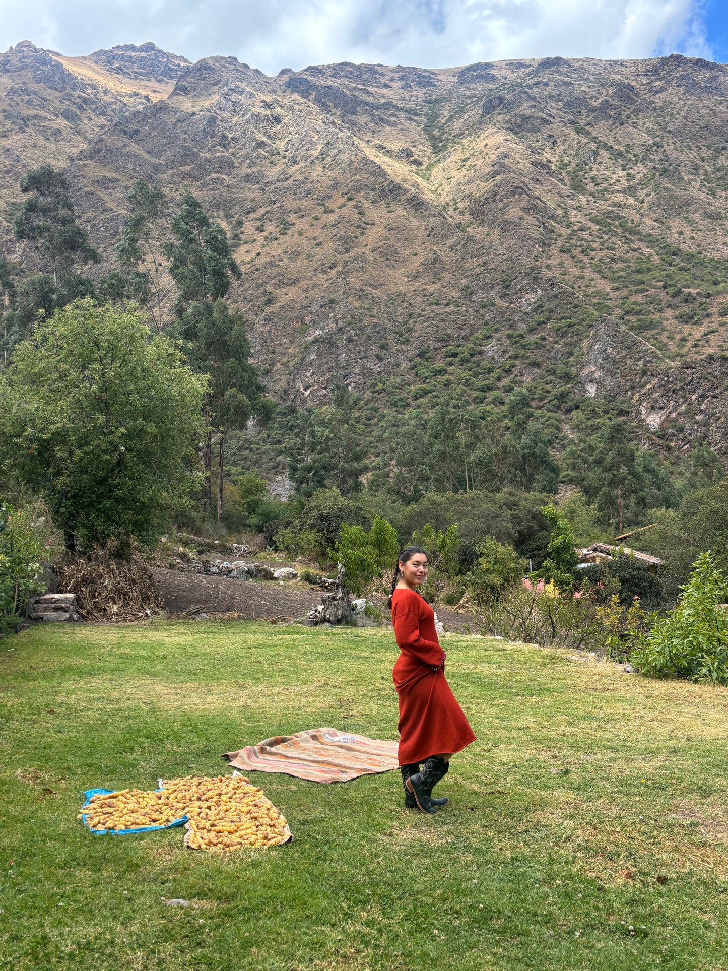 Woman wearing rust Rumi dress in 100% baby alpaca, embroidered with turquoise stones, standing in Peru's Sacred Valley of Urubamba.
