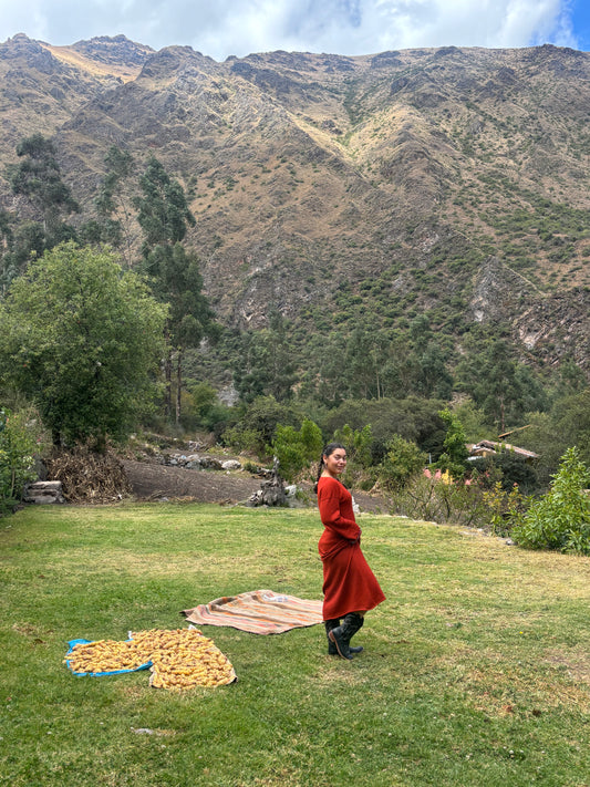 Woman wearing rust Rumi dress in 100% baby alpaca, embroidered with turquoise stones, standing in Peru's Sacred Valley of Urubamba.
